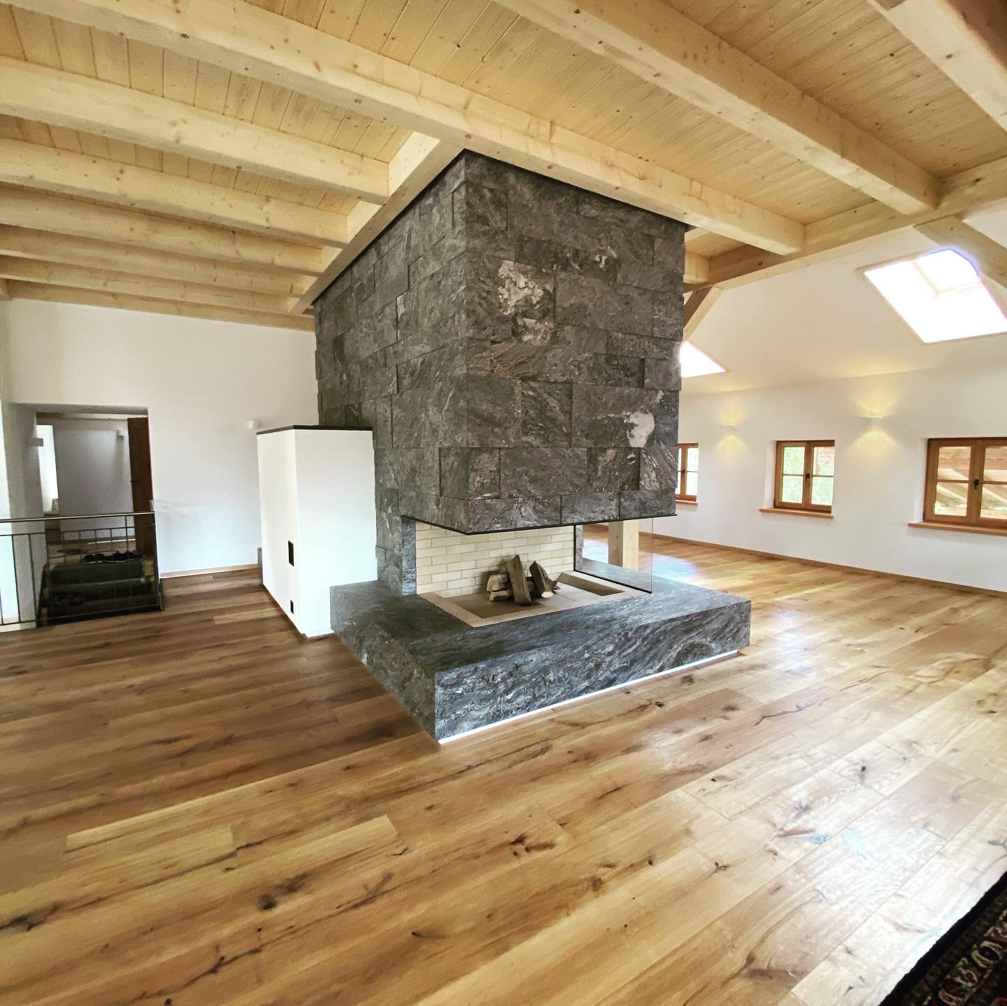 Landhaus Allgäu — Allgäu Gneis Kamin mit Holzbalkendecke — STOI Steinmetzwerkstatt