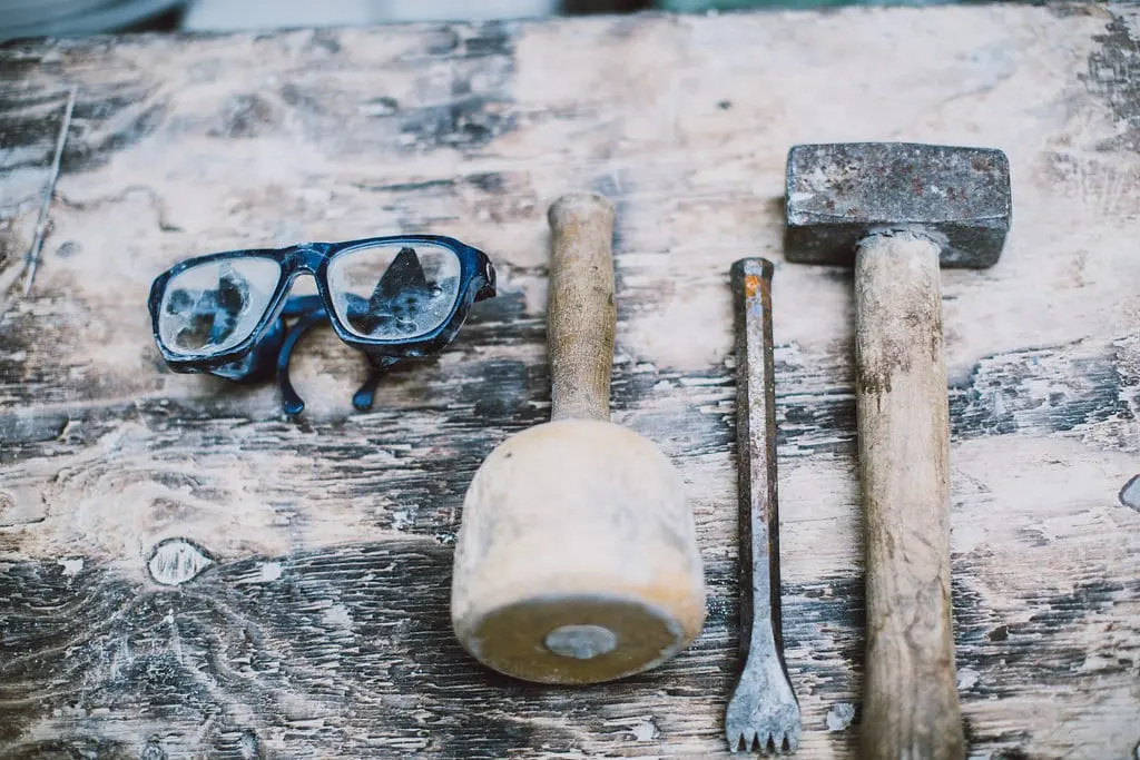 Knüpfel, Meißel, Fäustel und staubige Schutzbrille auf einer alten Holzwerkbank