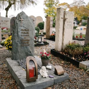 Dunkelgrauer Naturstein-Fels als Grabstein mit eingraviertem Kreuz und goldener Schrift, STOI