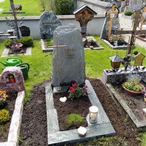Naturbelassener dunkelgrüner Diabas-Felsstein mit Goldkreuz auf dem Friedhof – STOI Steinmetzwerkstatt