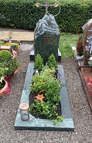 Felsengrabstein aus dunkelgrünem Naturstein in Bergform mit vergoldetem Kreuzornament an der Spitze