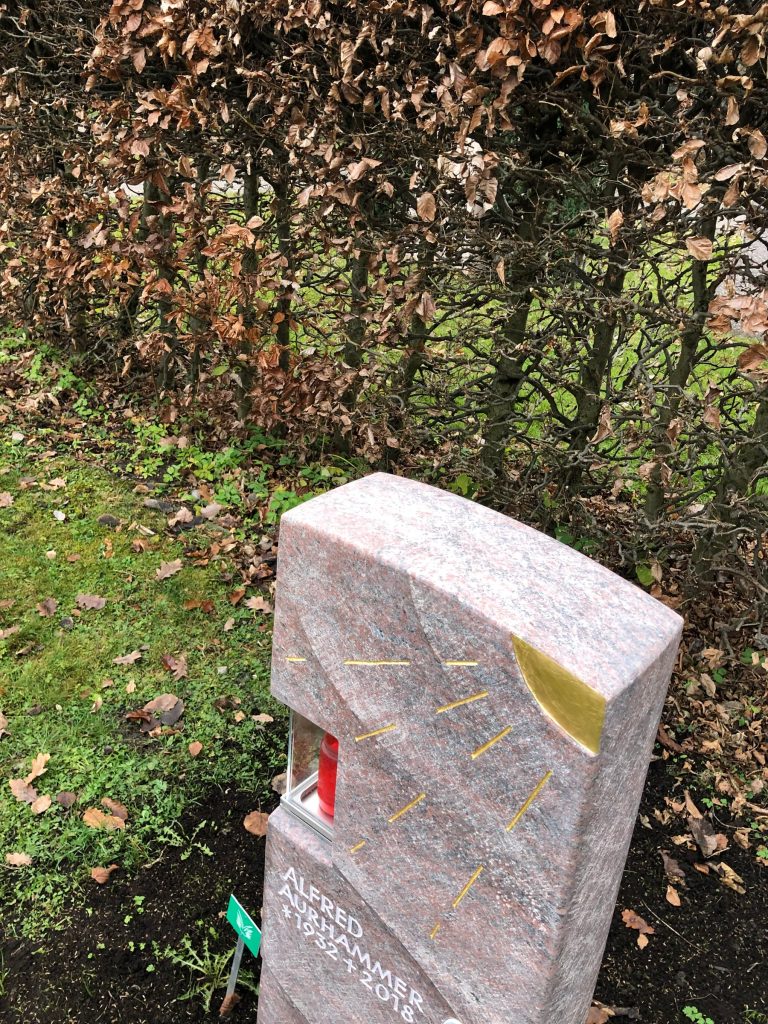 Warmroter Granit-Grabstein mit sandgestrahltem Sonnenmotiv, integrierter Kerze und Porträtmedaillon