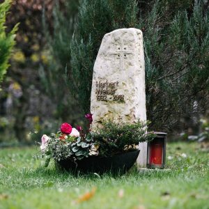 Naturbelassener Kalkstein-Findling als Grabstein mit eingravierten Kreuz und goldener Inschrift