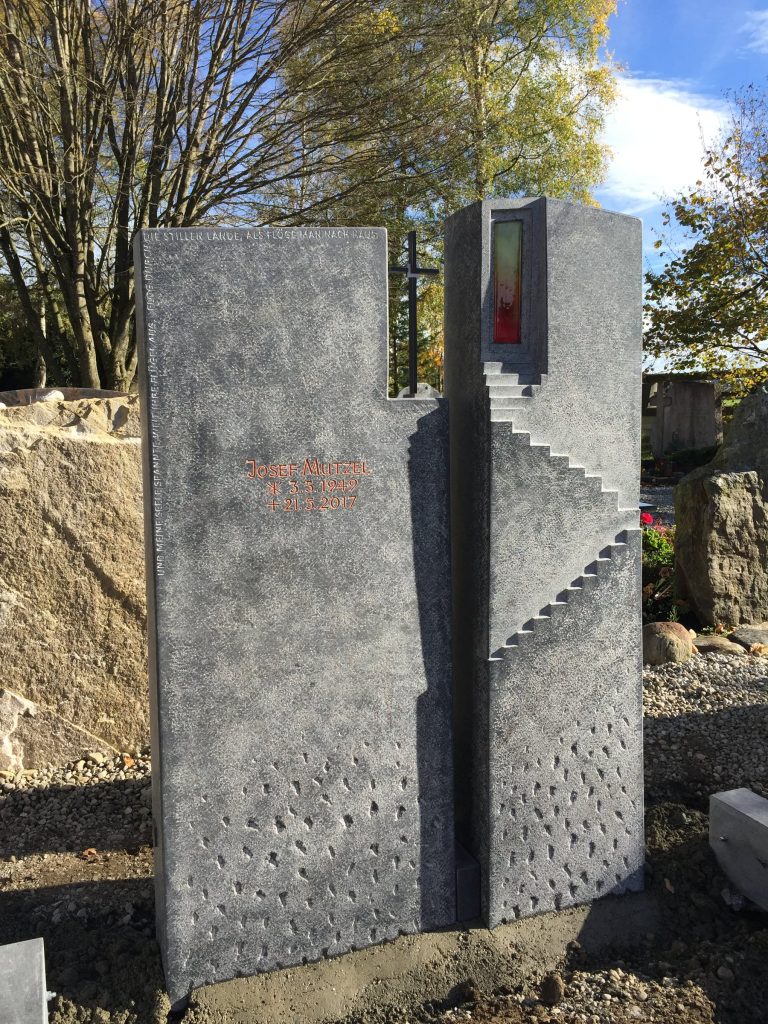 Mehrteiliger Grabstein aus dunklem Granit mit geometrischem Stufendesign und roter Glaseinlage