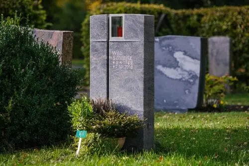 Grauer Granit-Grabstein mit vertikalem Kreuzschlitz und integrierter Glaskerze im oberen Bereich