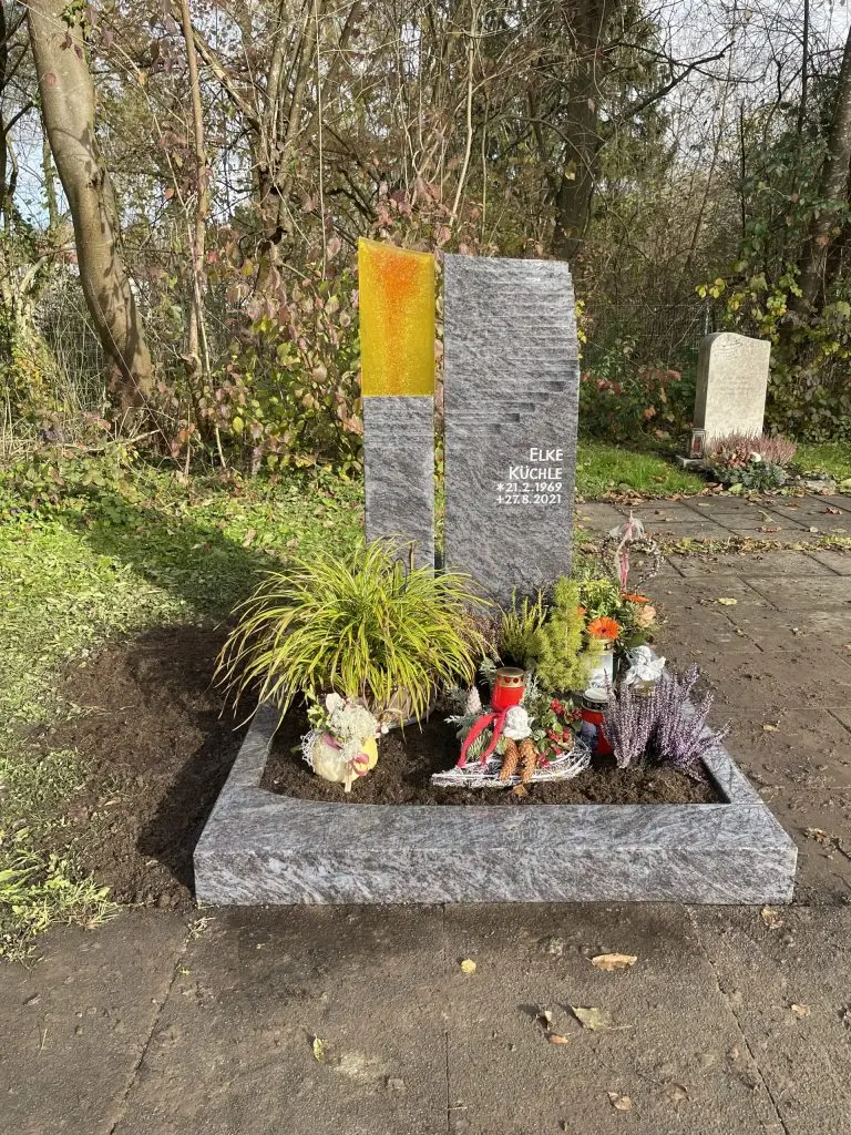 Moderner Grabstein aus dunklem Anthrazit-Granit mit leuchtend orangem Glas-Element und gestufter Oberkante