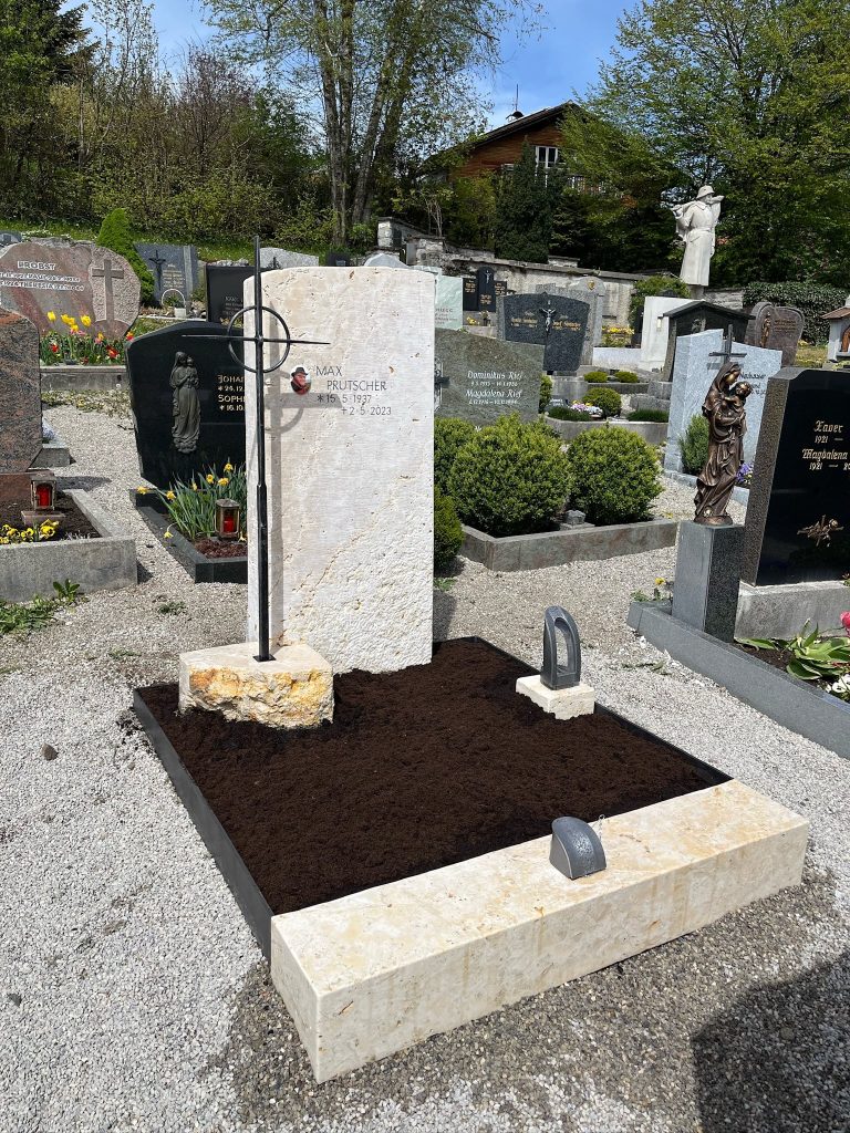 Heller Kalkstein-Grabstein mit schlanker Stele, naturbelassener Spaltbasis und aufgesetztem Metallkreuz