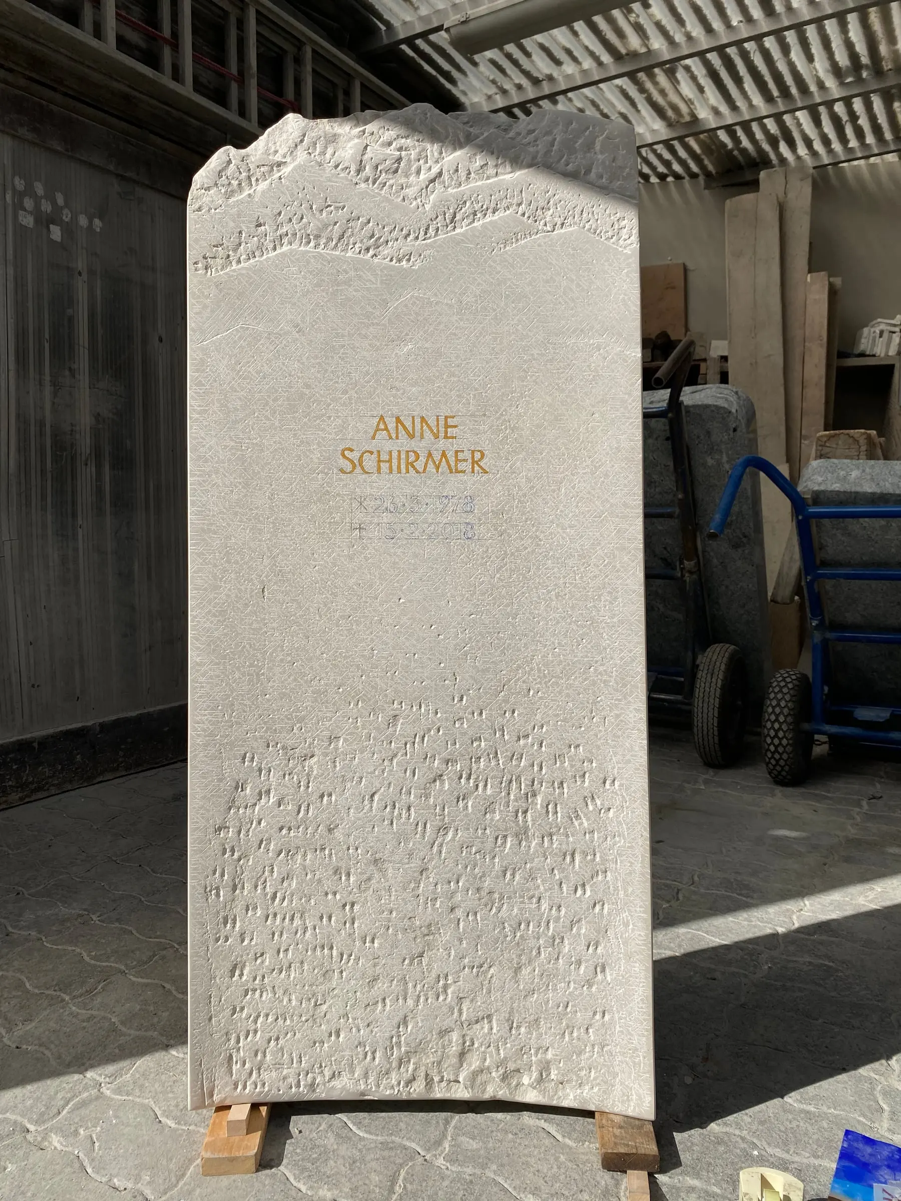 Helle schlanke Kalkstein-Stele mit Bergsilhouette als geschwungenem Abschluss von STOI Steinmetzwerkstatt