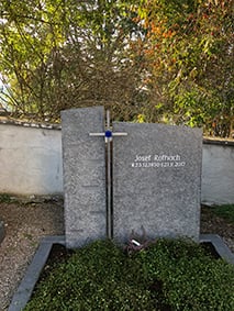 Hellgrauer Granit-Grabstein mit aufgesetztem Metallkreuz und leuchtendem blauen Glaseinsatz