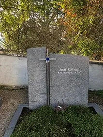 Hellgrauer Granit-Grabstein mit aufgesetztem Metallkreuz und leuchtendem blauen Glaseinsatz
