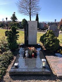 Zweiteiliges Grabmal aus hellem Kalkstein und dunklem Granit mit schlankem Metallkreuz von STOI
