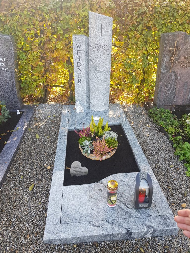 Zweiteilige Stele aus hellem Granit mit eingraviertem Kreuz und dunklem poliertem Liegestein