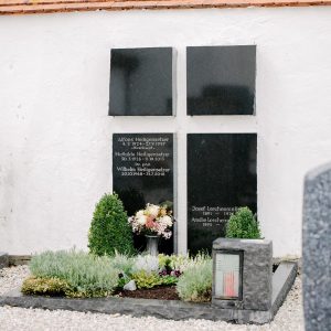 Wandgrabmal aus poliertem schwarzem Granit mit vier Tafeln im Kreuzformat an weißer Kirchenmauer