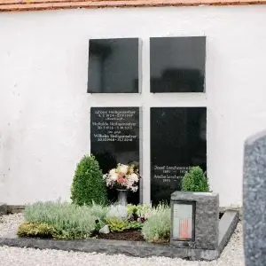 Wandgrabmal aus poliertem schwarzem Granit mit vier Tafeln im Kreuzformat an weißer Kirchenmauer