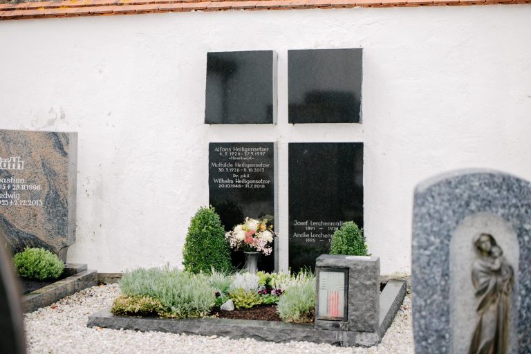 Wandgrabmal aus poliertem schwarzem Granit mit vier Tafeln im Kreuzformat an weißer Kirchenmauer