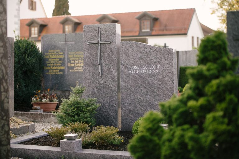 Zweiteiliger Grabstein aus dunkelgrauem Granit mit geschroteter Oberfläche und modernem Metallkreuz
