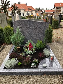 Polierter Grabstein aus anthrazitfarbenem Granit mit geschwungener Wellenform und Metallkreuz