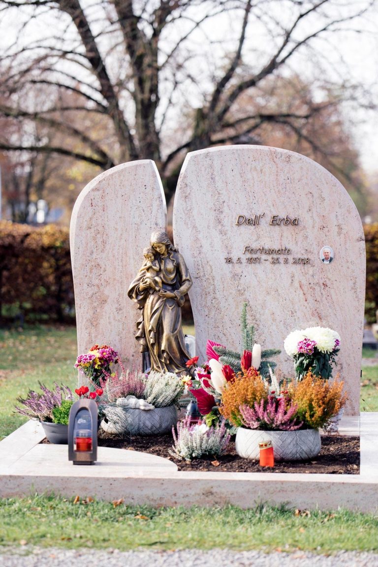 Zweiteiliger Grabstein aus rosafarbenem Kalkstein mit Rundbogen-Form und Bronzemadonna in der Mitte
