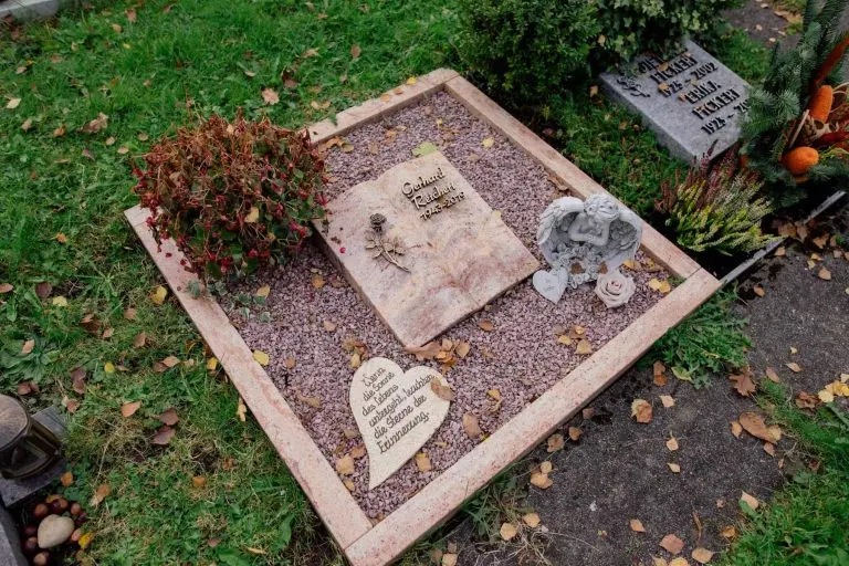 Urnengrab-Liegestein in rosa Naturstein mit Buch-Motiv, Engel-Figur und herzförmigem Stein auf Kiesanlage