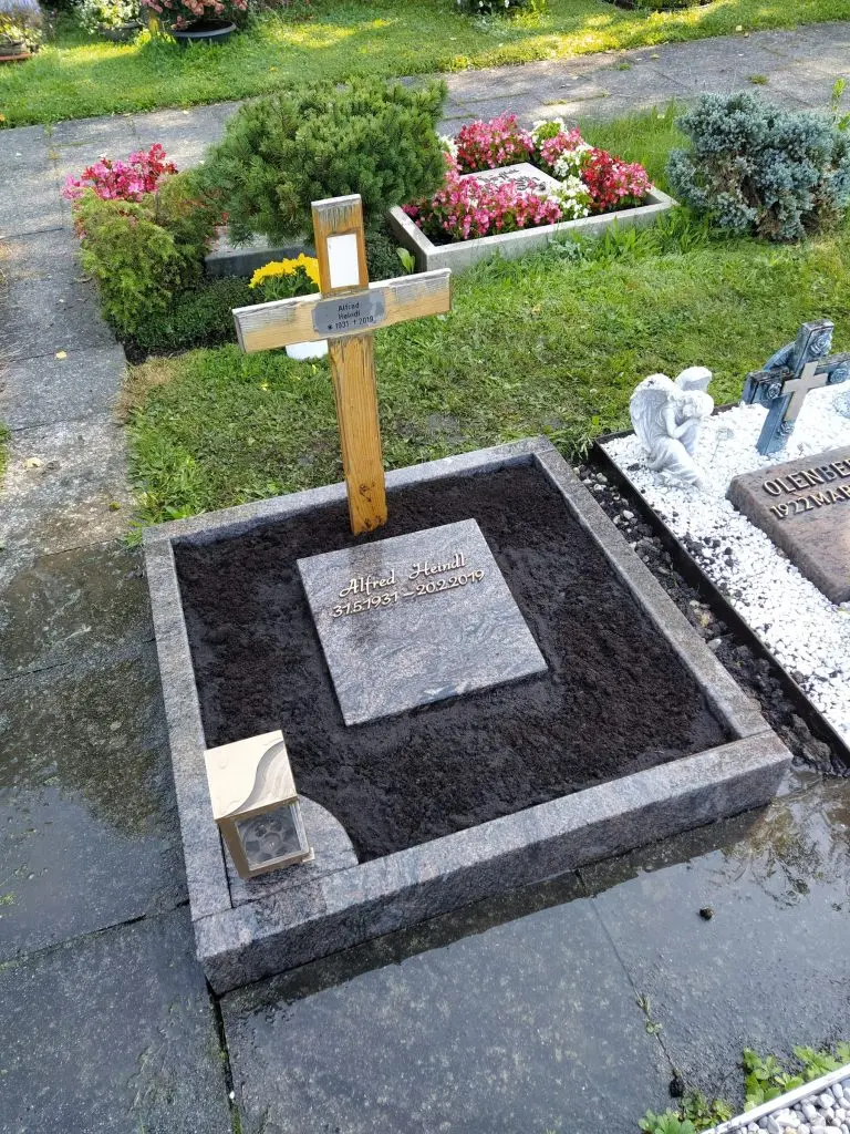 Flacher Urnenliegestein aus anthrazitfarbenem Granit mit polierter Inschriftfläche und Granitrahmeneinfassung