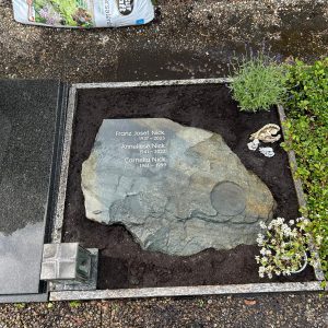 Natürlich geformter Fels-Liegestein aus grün-grauem Naturstein, flach liegend als Urnengrabstein